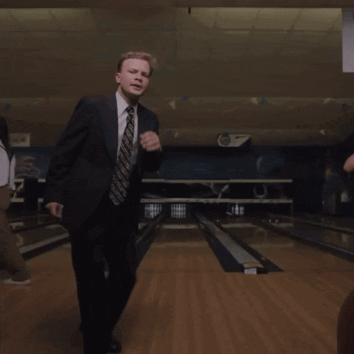 a man in a suit and tie is dancing in a bowling alley