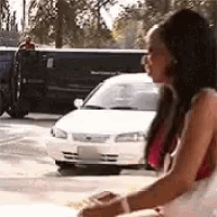 a woman is sitting on the side of the road in front of a car .