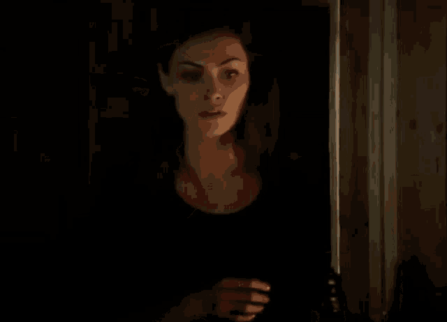 a woman is standing in a dark room holding a bottle of wine .