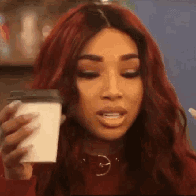a woman with red hair is holding a cup of coffee and making a face .