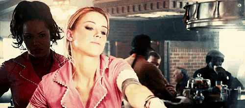 two women are sitting at a table in a diner . one of the women is wearing a pink shirt .