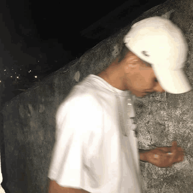 a man wearing a white hat and a white t-shirt is standing in front of a wall .