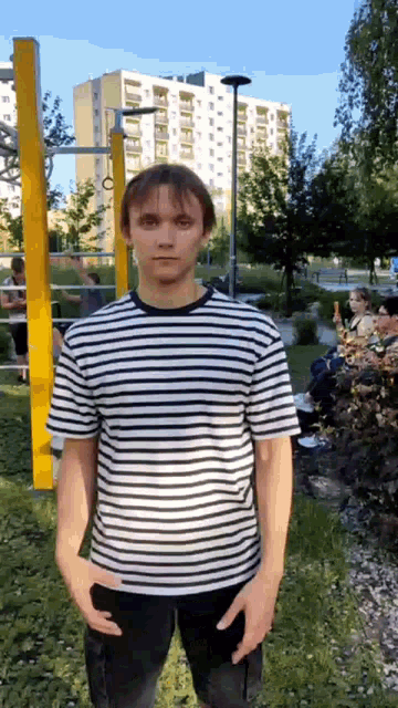 a man in a black and white striped shirt is standing in a park