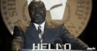 a man in a suit and tie is standing in front of a microphone and says hello