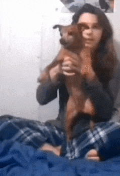 a woman is sitting on a bed holding a dog