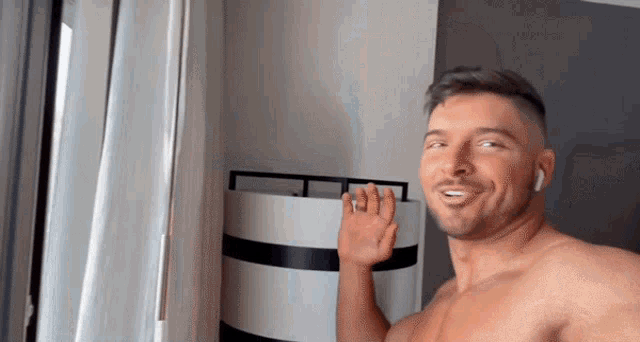 a shirtless man wearing ear buds is smiling and waving