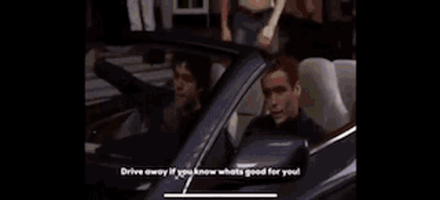 a man with a tattoo on his back is standing next to a car with the words drive away if you know whats good for you .