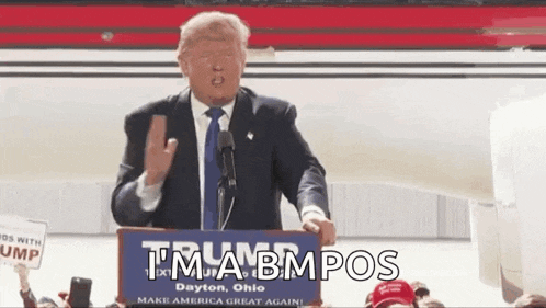 donald trump is giving a speech at a podium while holding a sign that says tma bmpos .
