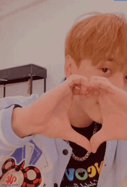 a young man making a heart shape with his hands and wearing a shirt that says vogu
