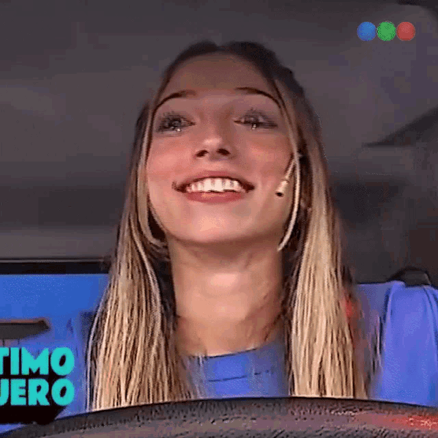 a woman in a blue shirt is smiling in front of a sign that says " timo "