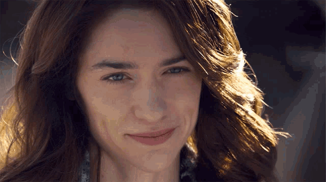 a woman with long brown hair and blue eyes is smiling