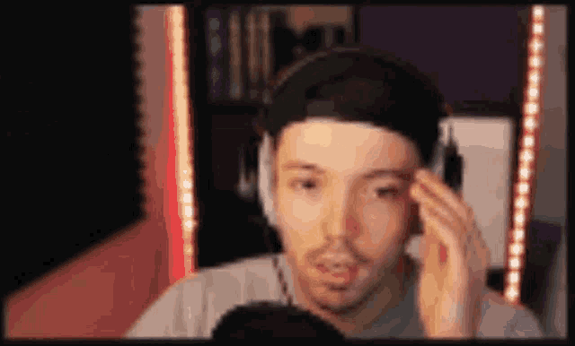 a man wearing headphones and a hat is talking into a microphone in front of a screen .