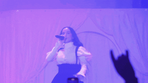 a woman singing into a microphone in front of a purple backdrop