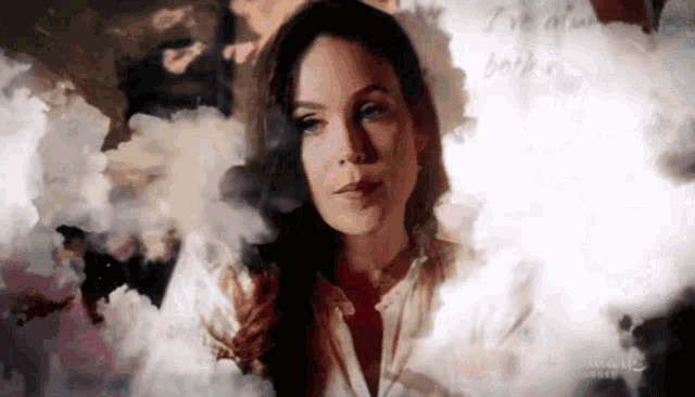 a woman in a white shirt is standing in front of a wall with smoke coming out of it .