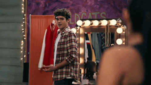 a man in a plaid shirt stands in front of a mirror with the word wildcats on the wall behind him