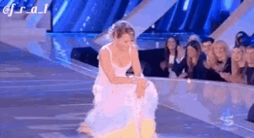 a woman in a white dress is kneeling down on a stage in front of a crowd of people .