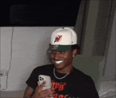 a man wearing a hat with devils on it is smiling while looking at his phone .