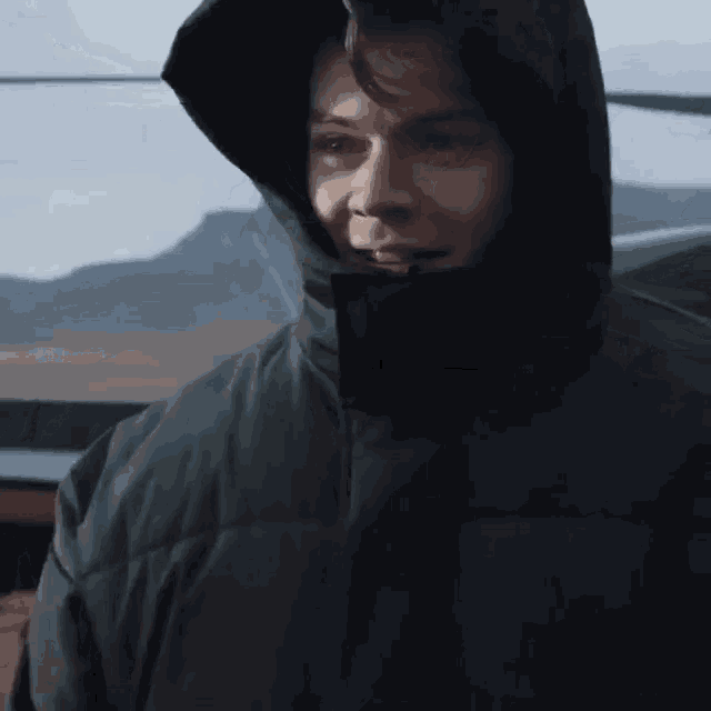 a man wearing a black jacket with a hood on his head is looking at the camera .