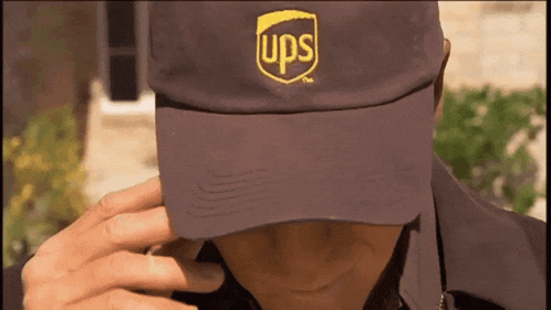 a man wearing a purple ups hat talks on a cell phone