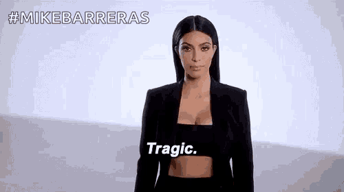 a woman in a black jacket and crop top is standing in front of a white background and says `` tragic '' .