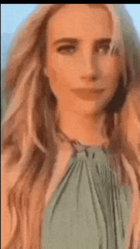 a close up of a woman 's face with long blonde hair and a green top .