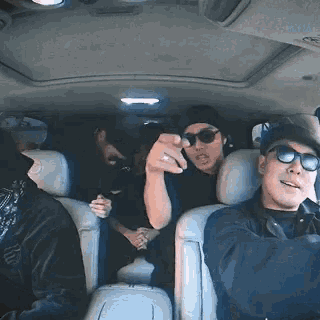 a man wearing sunglasses is pointing at the camera while sitting in a car