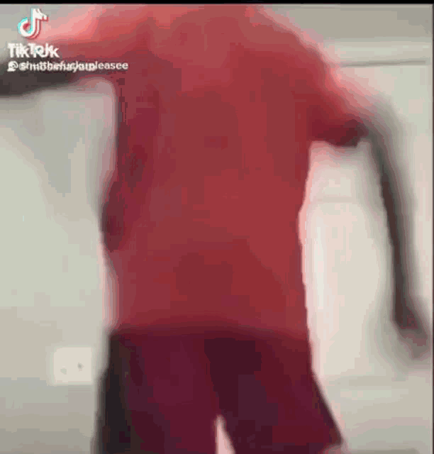 a man in a red shirt and shorts is standing in a room .