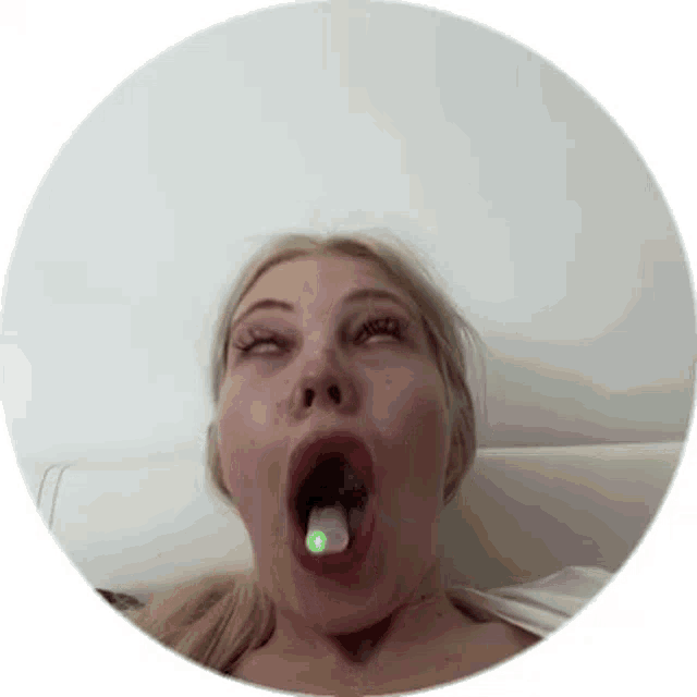 a woman is sitting on a bed with her mouth open and a green object in her mouth .