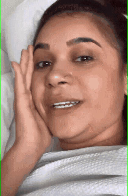 a woman with a nose ring is smiling while laying in bed