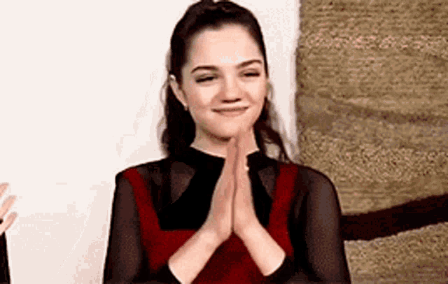 a woman in a red dress is sitting with her hands folded in prayer .