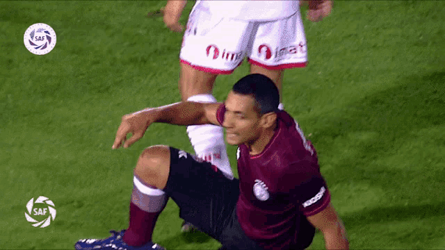 a soccer player in a maroon shirt is kneeling on the ground