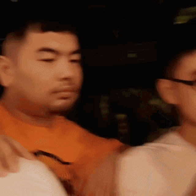 a man in an orange shirt and glasses is standing next to another man .