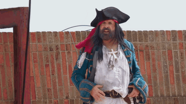 a man in a pirate costume stands in front of a red brick wall