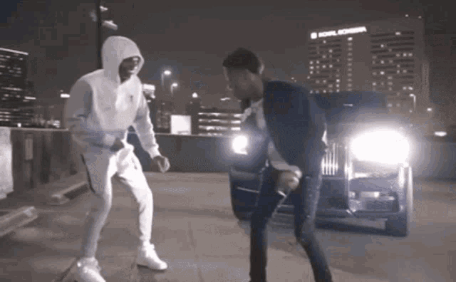 two men are dancing in front of a car with a building in the background that says bowl michigan