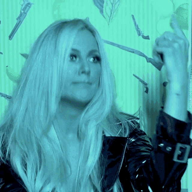 a woman in a black leather jacket is standing in front of a green wall with guns on it