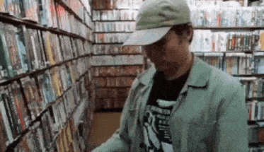 a man wearing a hat is standing in a book store looking at books .