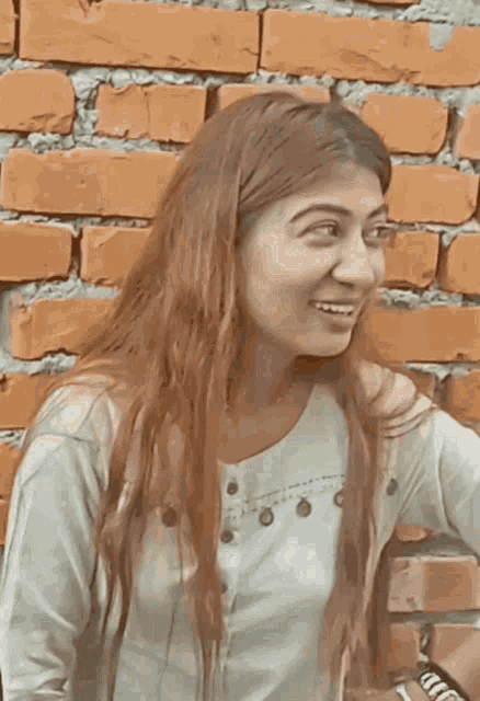 a woman standing in front of a brick wall smiles for the camera