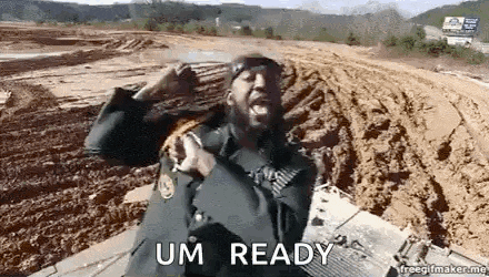 a man with a beard and a hat is standing in a dirt field .