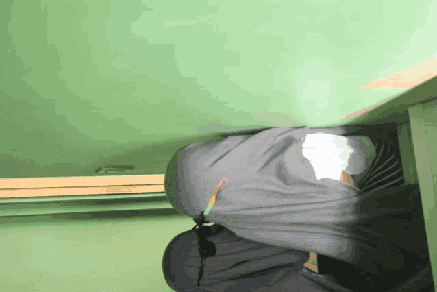 a person wearing a hijab is kneeling down with a green wall behind them