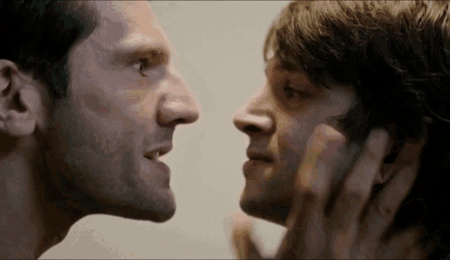 two men are looking at each other and one is touching his face