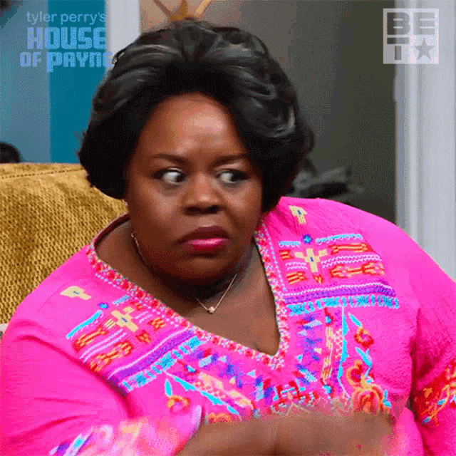 a woman in a pink shirt is sitting on a couch with a house of payne logo behind her