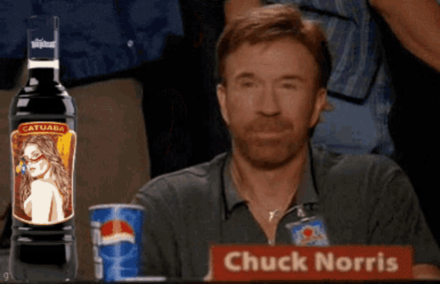 chuck norris is sitting at a table with a bottle of catuaba in front of him