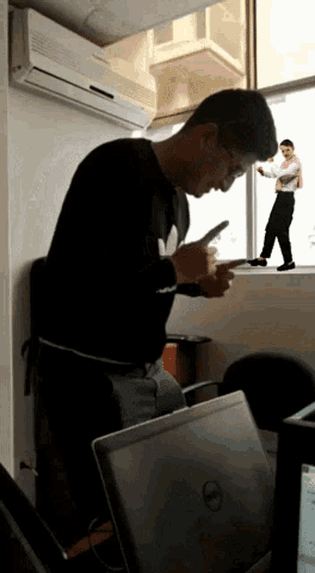 a man sitting in front of a dell laptop looking at a cell phone