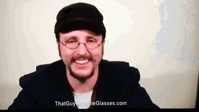 a man wearing glasses and a hat is smiling with the website thatguywiththeglasses.com in the background