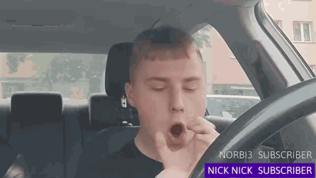 a man yawning while driving a car with a nick nick subscriber banner behind him