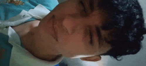 a young man with curly hair is laying down with his eyes closed and smiling .