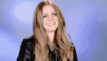a woman with long blonde hair is smiling and wearing a leather jacket .