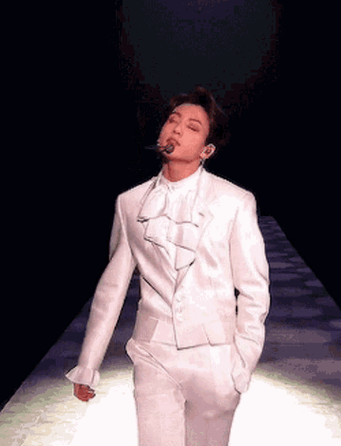 a man in a white suit is walking on a runway