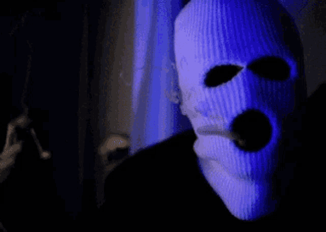 a man wearing a ski mask is smoking a cigarette in a dark room .