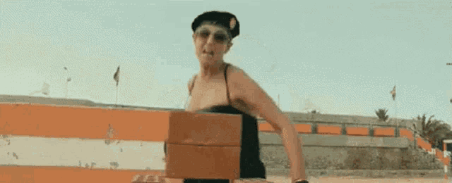 a woman in a bikini is standing next to an orange and white striped barrier holding a brick .